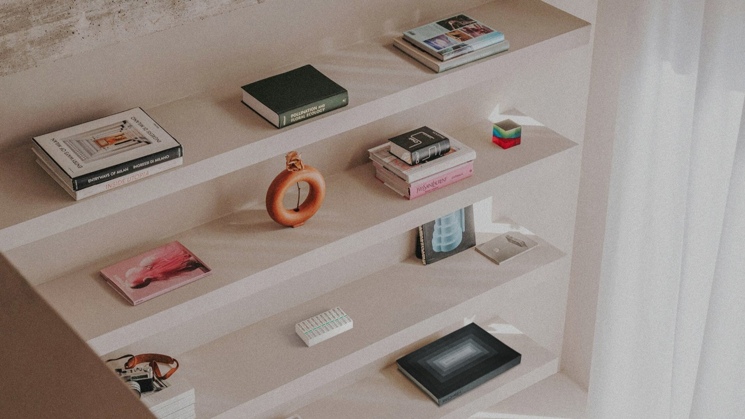 Shelves with various small items including books and decorative objects in a minimalistic setting. A 10-pack of NOAT and a NOAT book are blending in.
